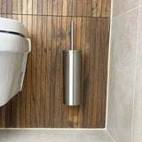 L'ensemble de toilettes Donato en acier inoxydable de yessential.fr est monté sur un mur avec des panneaux en bois à côté de toilettes blanches dans une salle de bains moderne avec sols et carrelages clairs.