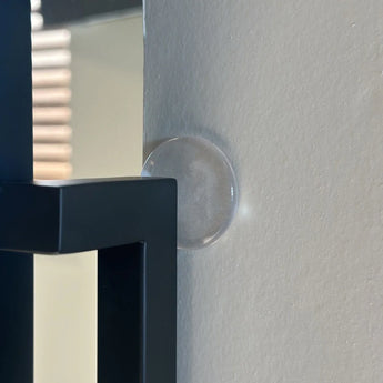 Le butoir de porte adhésif 6x ⌀2cm de yessential.fr adhère à un mur beige, afin qu'un miroir cerclé de noir ne touche pas et n'endommage pas la surface.