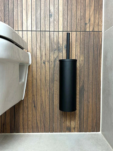 Une salle de bains moderne comprend des toilettes suspendues et le porte-brosse de toilette Branco Black avec brosse noire de yessential.fr, tous deux fixés à un mur en bois à côté de surfaces carrelées gris clair.