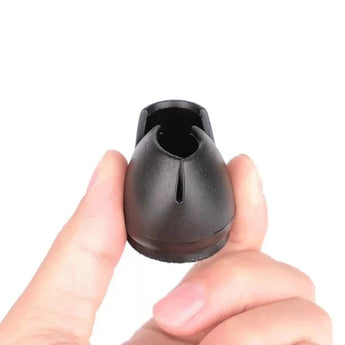 Une main tient un capuchon de pied de chaise Paco Set Ø 25-29 mm de yessential.fr, un petit protecteur de sol en plastique noir avec un dessus arrondi et une fente verticale, sur un fond blanc uni.