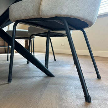 Gros plan de chaises modernes avec coussins légers et pieds en métal noir, équipées des protège-pieds de chaise Paco Set Ø 21-25 mm de yessential.fr pour la protection du sol, sur un parquet dans une pièce lumineuse et minimaliste.