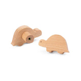 Les boutons de tiroir Bambino Dino de yessential.fr comportent deux tortues en bois clair - l'une montrant un profil latéral, l'autre une vue arrière avec vis en métal - idéales comme bouton de meuble en bois pour la chambre des enfants.