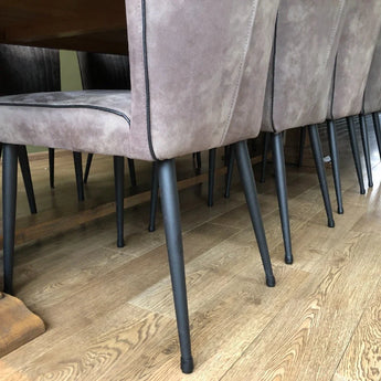 Un gros plan montre des chaises de salle à manger rembourrées avec des pieds en métal noir, équipées de protège-pieds anti-rayures Paco Set Ø 17-21 mm de yessential.fr, disposées autour d'une table à manger en bois sur un parquet en bois clair.