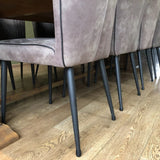 Une rangée de chaises de salle à manger rembourrées gris-brun avec des pieds en métal noir, chacune équipée des embouts de pieds de chaise en feutre anti-rayures Paco Set Ø 25-29 mm de yessential.fr, entoure une table en bois sur un plancher en bois marron clair.