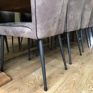Un gros plan de chaises de salle à manger modernes avec des sièges gris clair et des pieds en métal noir équipés de l'ensemble Paco yessential.fr Ø 12-16 mm, disposées autour d'une table à manger en bois sur un parquet marron clair.