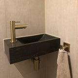Une serviette de couleur claire est suspendue à l'ensemble de toilette Verano Gold en or brossé de yessential.fr, ajoutant une élégance subtile à ces accessoires de toilette de couleur dorée.