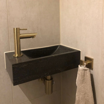 Une serviette de couleur claire est suspendue à l'ensemble de toilette Verano Gold en or brossé de yessential.fr, ajoutant une élégance subtile à ces accessoires de toilette de couleur dorée.