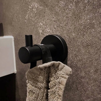 Une texture de serviette beige est suspendue à un crochet Justo Black de yessential.fr, fixé au mur et pierre grise, avec une surface claire visible d'un seul coup d'oeil.