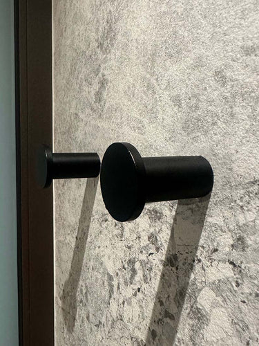 Quatre crochets à serviettes cylindriques noirs Carreno de yessential.fr, en acier inoxydable, sont montés sur un mur texturé en pierre grise - un accessoire de salle de bain élégant et moderne.