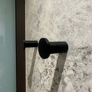 Quatre crochets à serviettes cylindriques noirs Carreno de yessential.fr, en acier inoxydable, sont montés sur un mur texturé en pierre grise - un accessoire de salle de bain élégant et moderne.