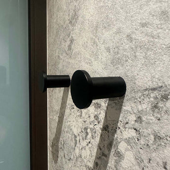 Quatre crochets à serviettes cylindriques noirs Carreno de yessential.fr, en acier inoxydable, sont montés sur un mur texturé en pierre grise - un accessoire de salle de bain élégant et moderne.