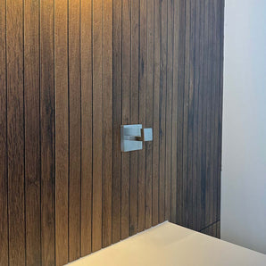 Un crochet porte-serviettes en acier inoxydable doté d'une rosace carrée est monté sur un panneau de bois vertical.