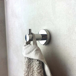 Le crochet Justo Chrome de yessential.fr est monté sur un mur légèrement carrelé et peut contenir une serviette beige et un gant de toilette texturé - un ajout élégant et pratique à n'importe quelle salle de bain.
