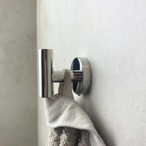 Un gros plan montre le crochet Rodrigo Chrome yessential.fr, un accessoire de salle de bain cylindrique moderne, solidement monté et tenant une serviette texturée beige contre un mur de couleur claire.