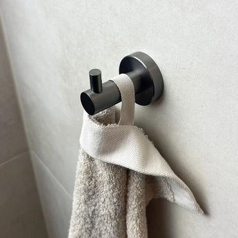L'ensemble WC Romano Gunmetal de yessential.fr, de notre collection d'accessoires de salle de bain de luxe, contient une serviette blanche avec une boucle en tissu et s'accroche élégamment contre un mur carrelé gris clair.
