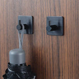 Deux crochets Navarro Black de yessential.fr sont montés sur bois. Sur un crochet se trouve la boucle d'un parapluie noir fermé avec une poignée grise ; l'autre crochet est vide.