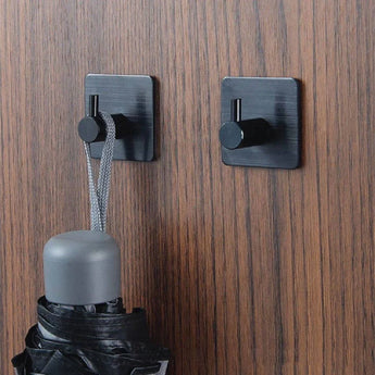 Deux crochets Navarro Black de yessential.fr sont montés sur bois. Sur un crochet se trouve la boucle d'un parapluie noir fermé avec une poignée grise ; l'autre crochet est vide.
