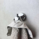 Une serviette texturée grise est suspendue au crochet Justo Chrome de yessential.fr, monté sur un mur lisse gris clair.