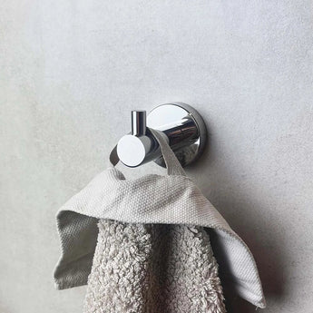 Une serviette texturée grise est suspendue au crochet Justo Chrome de yessential.fr, monté sur un mur lisse gris clair.