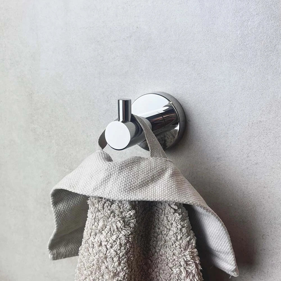 Une serviette texturée grise est suspendue au crochet Justo Chrome de yessential.fr, monté sur un mur lisse gris clair.