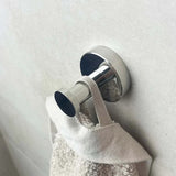 Un gros plan de l'ensemble WC Santino Chrome de yessential.fr - un crochet mural brillant de la gamme d'accessoires de salle de bain - retenant une serviette de couleur claire avec une boucle en tissu, monté sur un mur de salle de bain lisse et clair.