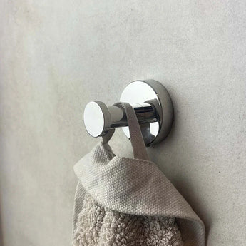 L'ensemble de toilette Cosimo Chrome de yessential.fr continue avec une serviette beige avec boucle et carrelage avec une surface texturée grise, au look simple et minimal, idéal pour les accessoires de la salle de bain représenté.