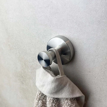 Le crochet et l'inox Kyano de yessential.fr maintiennent une serviette beige avec la boucle sur un fond gris blanc clair et apportent un style moderne au bain.