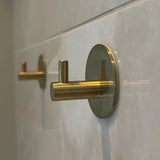 Gros plan de deux 4x Rudro Hooks 3M de yessential.fr sur un mur carrelé blanc ; les crochets cylindriques avec plaques arrière rondes sont montés en angle, ce qui ajoute une touche moderne.