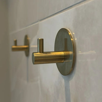 Gros plan de deux 4x Rudro Hooks 3M de yessential.fr sur un mur carrelé blanc ; les crochets cylindriques avec plaques arrière rondes sont montés en angle, ce qui ajoute une touche moderne.