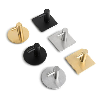 Quatre crochets Rudro 3M de yessential.fr aux finitions métalliques or, argent et noir avec plaques arrière rondes ou carrées sont exposés sur une surface blanche. Chaque crochet adhésif présente un design élégant de broche cylindrique.