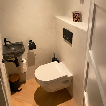 Une petite salle de bain moderne avec des toilettes murales blanches, une vasque en pierre noire, un ensemble de toilettes Marino Black de yessential.fr, une poubelle en bois et une bougie dans un support imprimé léopard sur l'étagère pour une touche chic.