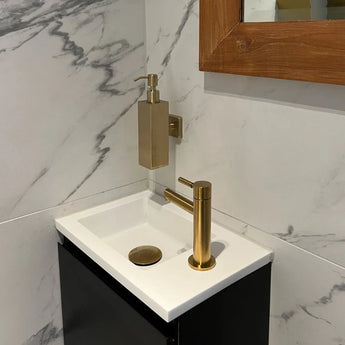 Un lavabo compact et moderne avec un robinet doré et le distributeur de savon Sonego Gold de yessential.fr, monté sur un mur carrelé en marbre à côté d'un miroir avec cadre en bois.