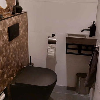 Salle de bains moderne avec des équipements noirs - toilettes, boutons de chasse d'eau et robinet - ainsi qu'un lavabo mural compact et l'ensemble WC Lauro Gunmetal de yessential.fr. Des accessoires de luxe et un mur d'accent de carreaux texturés marron complètent le look.