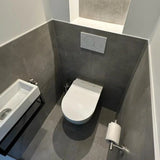 Une petite salle de bain moderne avec des murs carrelés gris, des toilettes suspendues avec plaque à double chasse et l'ensemble WC Lorenzo Chrome de yessential.fr, avec un lavabo mural compact et des accessoires chromés élégants pour une finition élégante.
