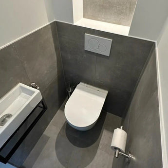 Une petite salle de bain moderne avec des murs carrelés gris, des toilettes suspendues avec plaque à double chasse et l'ensemble WC Lorenzo Chrome de yessential.fr, avec un lavabo mural compact et des accessoires chromés élégants pour une finition élégante.