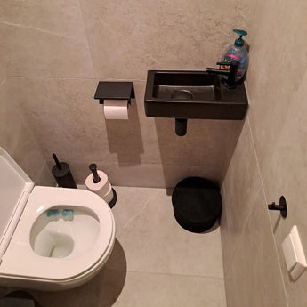 Une petite salle de bain moderne avec des toilettes blanches, l'ensemble WC Juano Black (sans perçage) de yessential.fr, un lavabo noir compact avec du savon et un tapis rond noir sur carrelage gris clair.