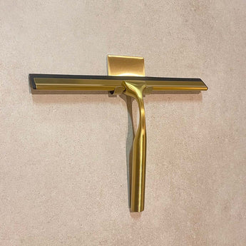 De Zamoro Gold van yessential.fr, met een gouden handvat en zwart blad, is verticaal gemonteerd op een muur met beige structuur en een 3M ophangsysteem.