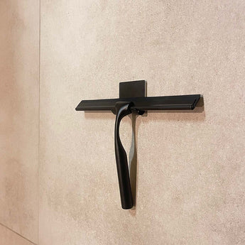 Une extracteur de douche Zamoro Black de yessential.fr est accrochée à un support mural avec un système de suspension 3M contre un mur carrelé beige.