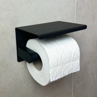 Un rouleau de papier toilette blanc gaufré est monté sur le porte-rouleau papier toilette Tazio Black de yessential.fr, qui est fixé sur un mur carrelé de couleur claire.