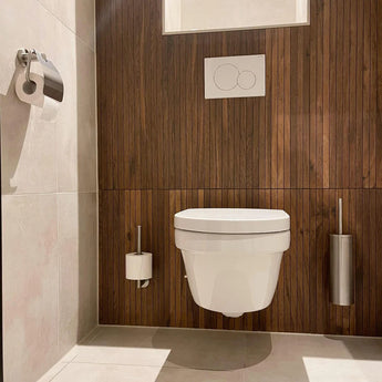 Salle de bain moderne avec toilettes suspendues blanches, panneau mural en bois, bouton de chasse d'eau double et ensemble de toilettes Lauro en acier inoxydable de yessential.fr - composé d'une brosse de toilettes, d'un porte-papier toilette et d'une poubelle - sur sols et murs légèrement carrelés.