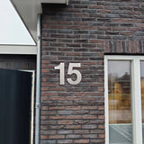 Le chiffre 15 est écrit en grands chiffres de 30 cm en acier inoxydable Adamo argenté de yessential.fr sur le mur extérieur en brique d'un bâtiment à côté d'une fenêtre.
