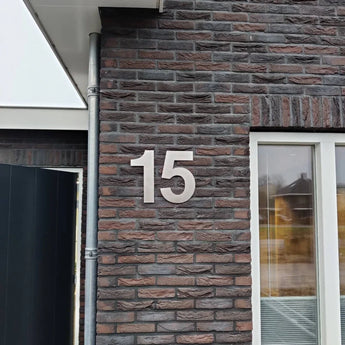 Le chiffre 15 est écrit en grands chiffres de 30 cm en acier inoxydable Adamo argenté de yessential.fr sur le mur extérieur en brique d'un bâtiment à côté d'une fenêtre.