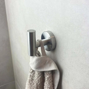 Un crochet Rodrigo en acier inoxydable de yessential.fr maintient une serviette beige texturée contre un mur de salle de bains carrelé gris clair.