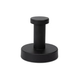 Un élégant butoir de porte cylindrique en métal noir avec une base ronde et un dessus plat de yessential.fr - un complément idéal avec votre ensemble WC Xavo Black ou d'autres accessoires de salle de bain noir mat. Photographié sur un fond blanc.