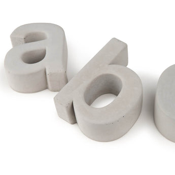 Deux lettres minuscules en béton 3D « a » et « b » (Enrico béton 30 cm par yessential.fr) sont sur fond blanc, le « b » étant couché sur le côté et partiellement découpé de l'image.