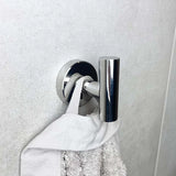 Une serviette blanche est suspendue à la boucle de l'ensemble WC Nando Chrome de yessential.fr, avec un crochet mural argenté brillant se détachant sur un mur gris clair.