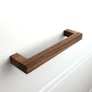 La poignée de tiroir Vasco Walnut de yessential.fr, au design rectangulaire moderne et minimaliste, est fixée à une porte d'armoire blanche.