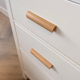 Gros plan de poignées en chêne dans un style minimaliste moderne. Les tiroirs font partie d'un placard posé sur un parquet en bois clair.