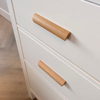 Gros plan de poignées en chêne dans un style minimaliste moderne. Les tiroirs font partie d'un placard posé sur un parquet en bois clair.