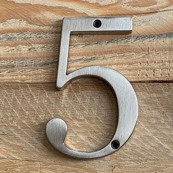 Le Matteo Nickel 10cm de yessential.fr, avec une finition en métal brossé, se fixe sur une surface en bois clair à l'aide de deux vis - une au dessus et une en dessous du chiffre 5.